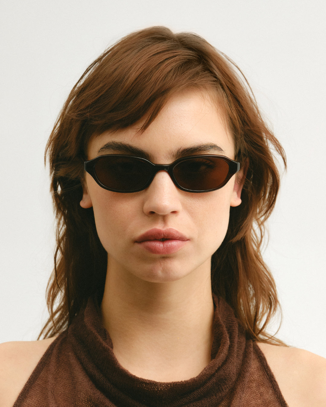 Female model wearing Corlin Eyewear Aidan Brown Brown sunglasses — front view of slim square acetate frame and German OBE hinges