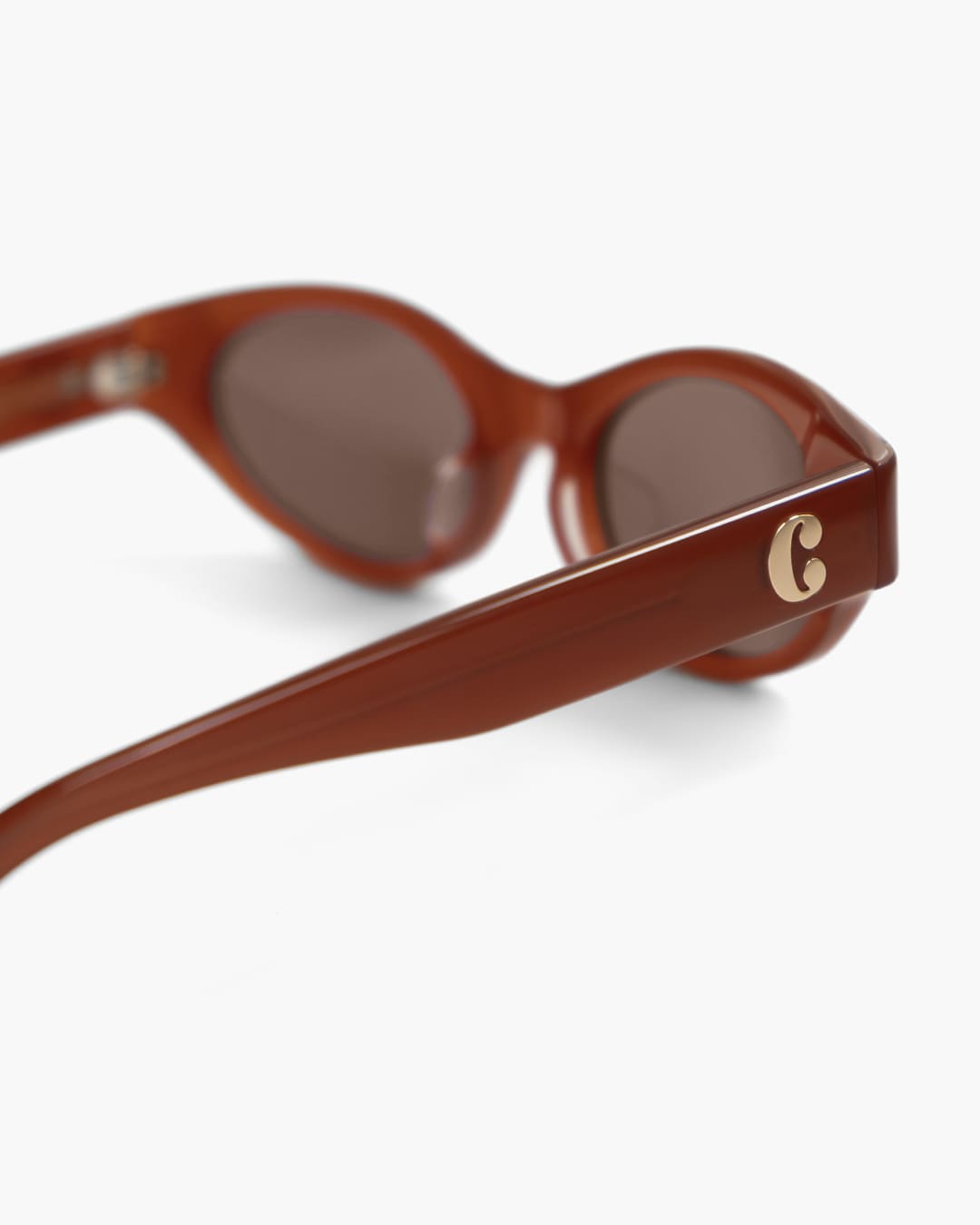 Red brown sunglasses from the side with focus on the logo on a white background