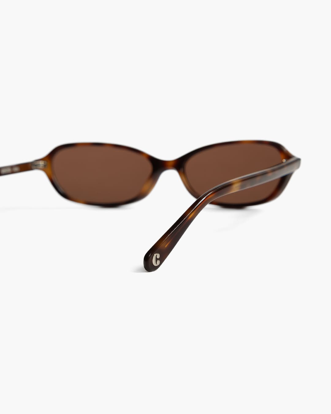 Sunglasses with tortoiseshell frame and brown lenses on a white background with focus on the back