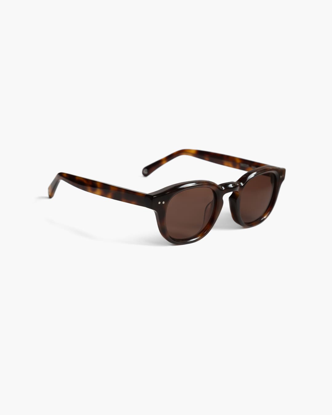 Sunglasses with tortoiseshell frame and dark lenses on a white background slightly from the side