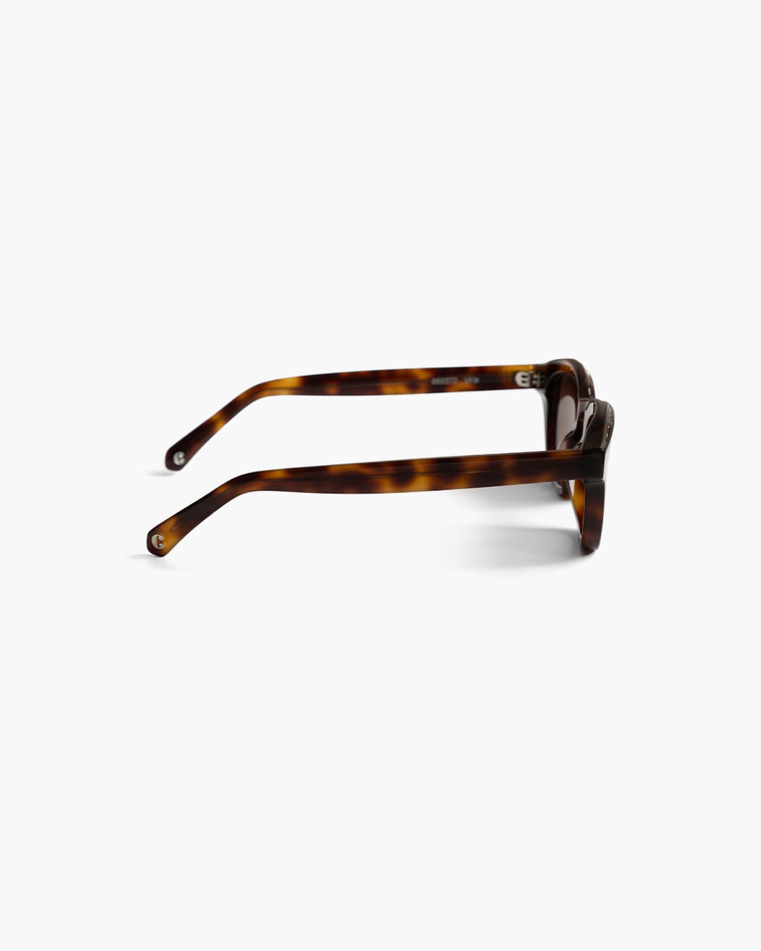 Sunglasses with tortoiseshell frame and dark lenses on a white background from the side