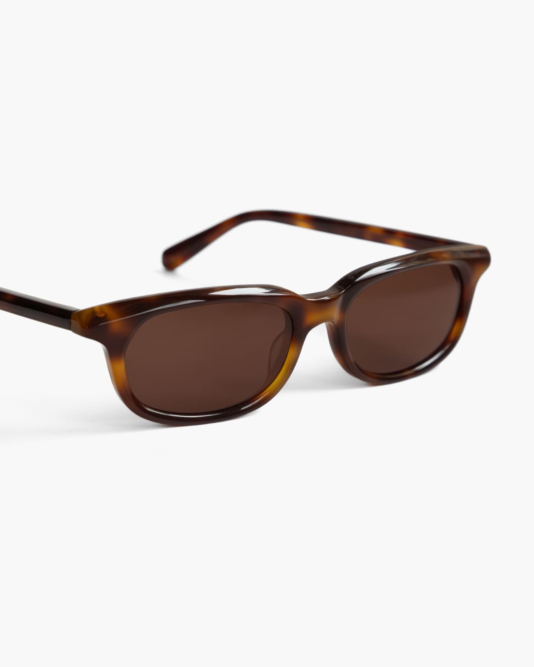 Closeup of sunglasses with tortoiseshell frame and brown lenses on a white background