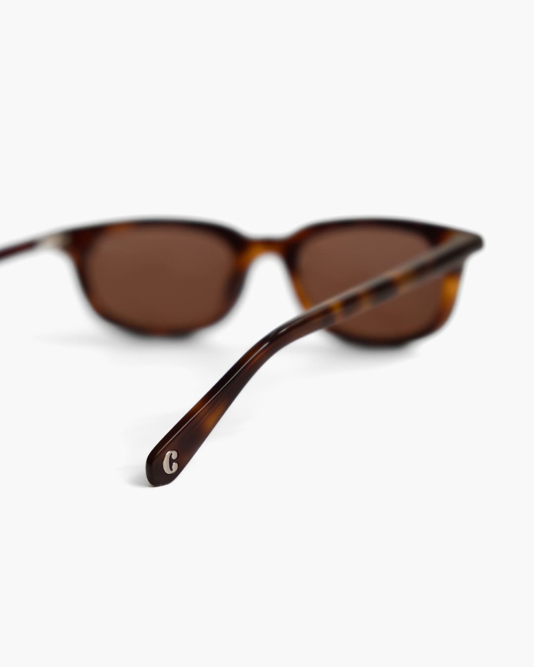 Brown sunglasses with tortoiseshell frame from the back on a blurred white background with focus on the logo