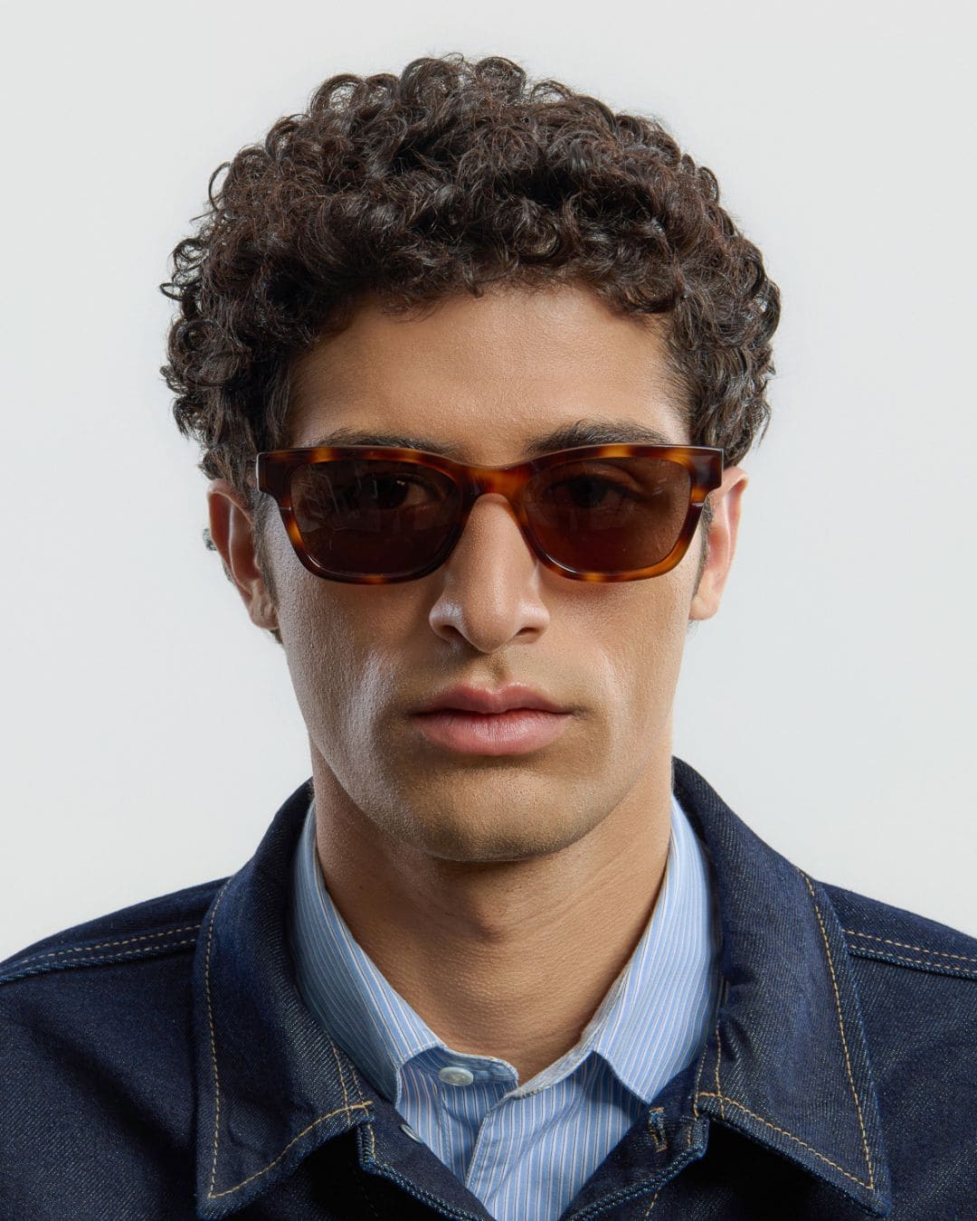 Man wearing tortoise brown sunglasses with a neutral background