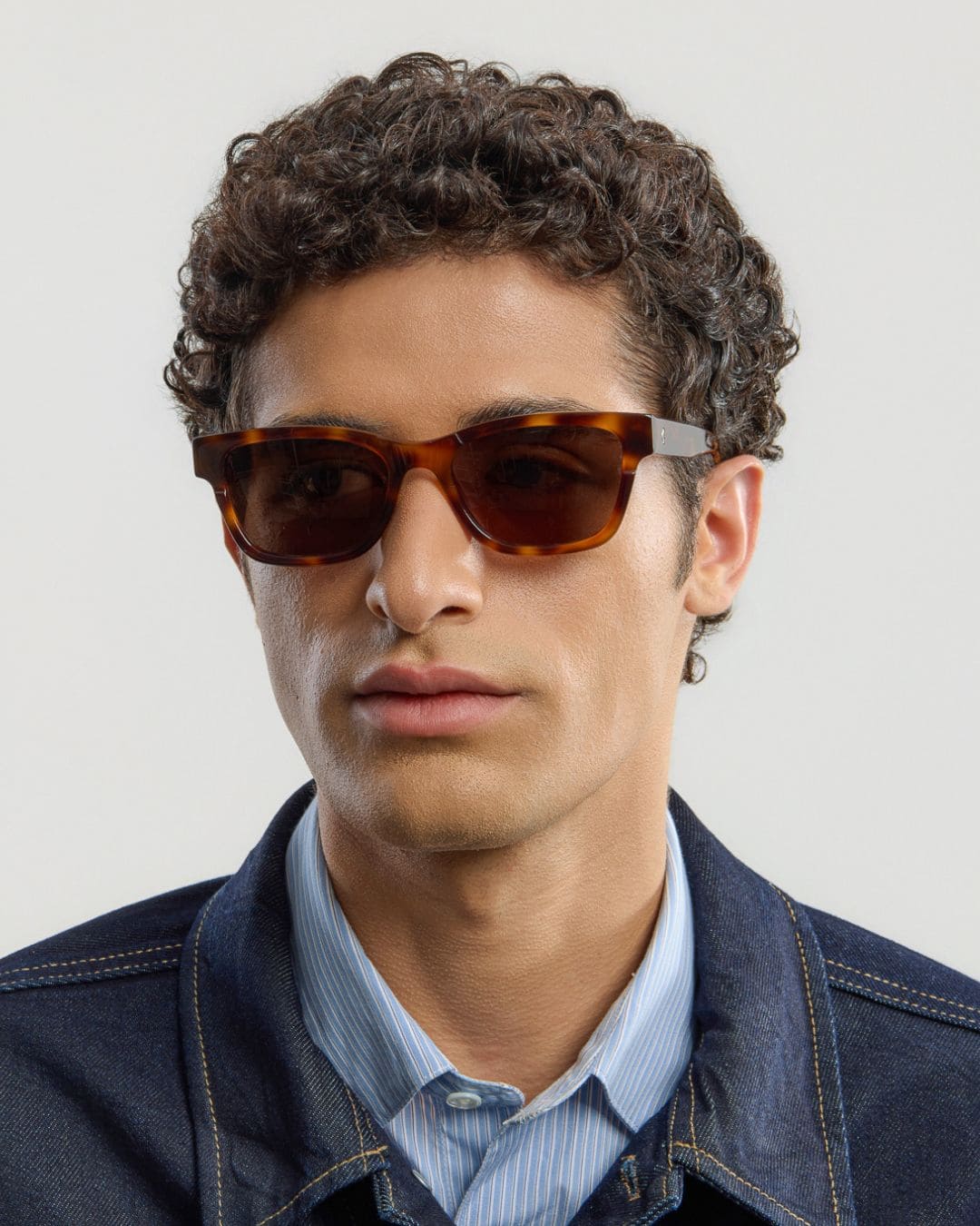 Man wearing tortoise brown sunglasses with a neutral background