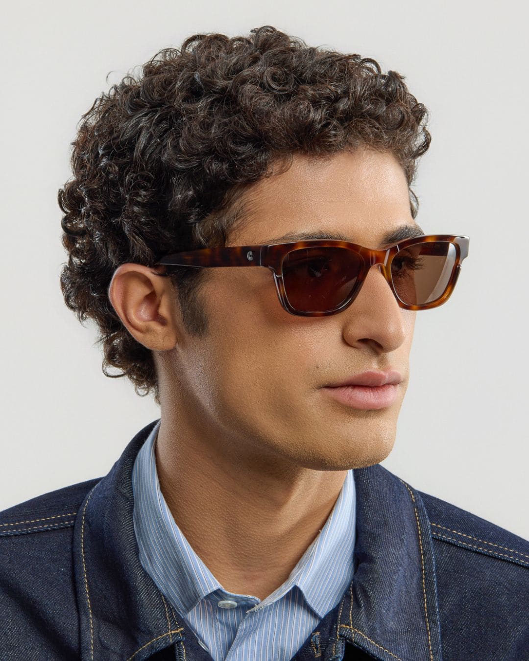 Man wearing tortoise brown sunglasses with a neutral background