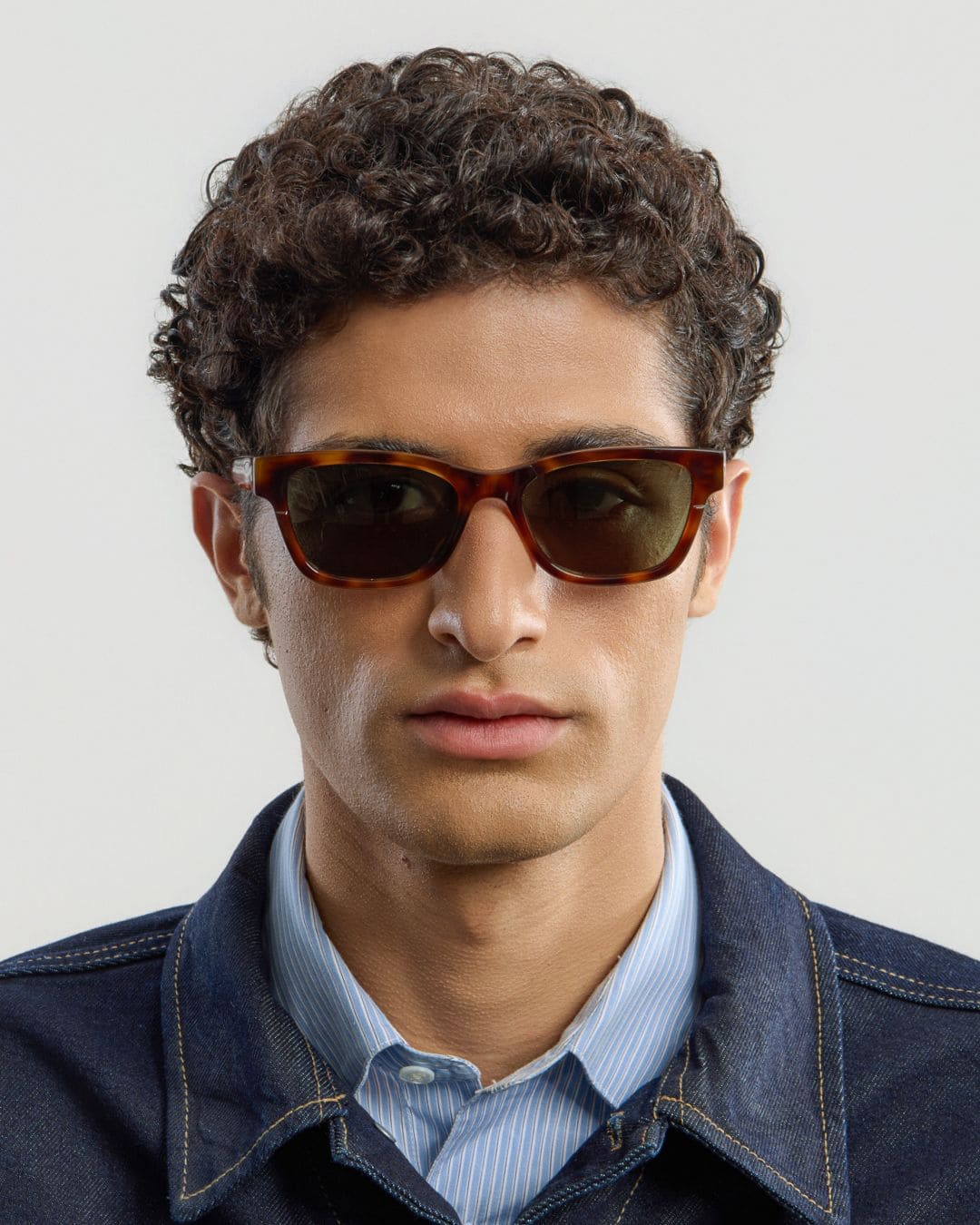 Man wearing tortoise green sunglasses with a neutral background