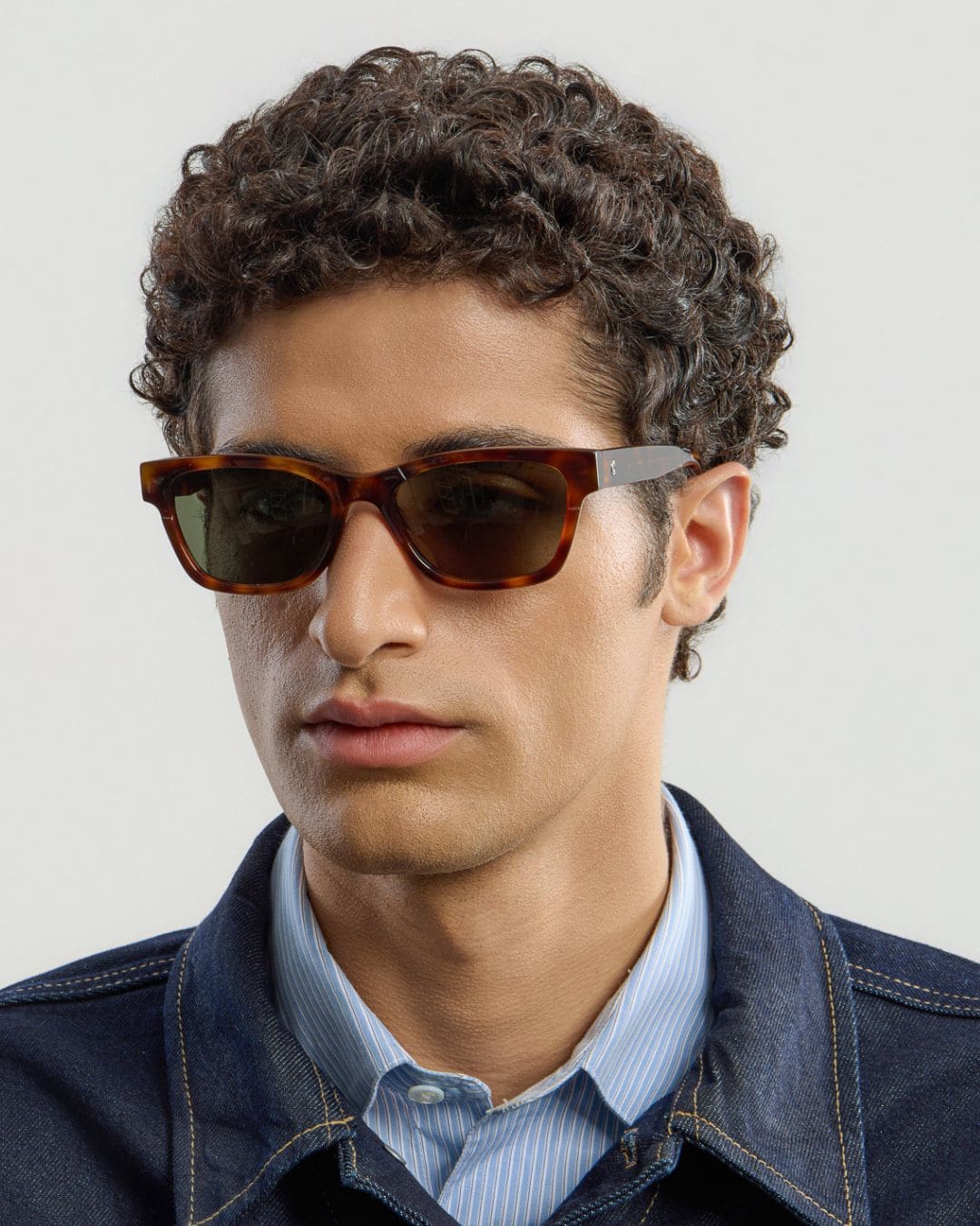 Man wearing tortoise green sunglasses with a neutral background