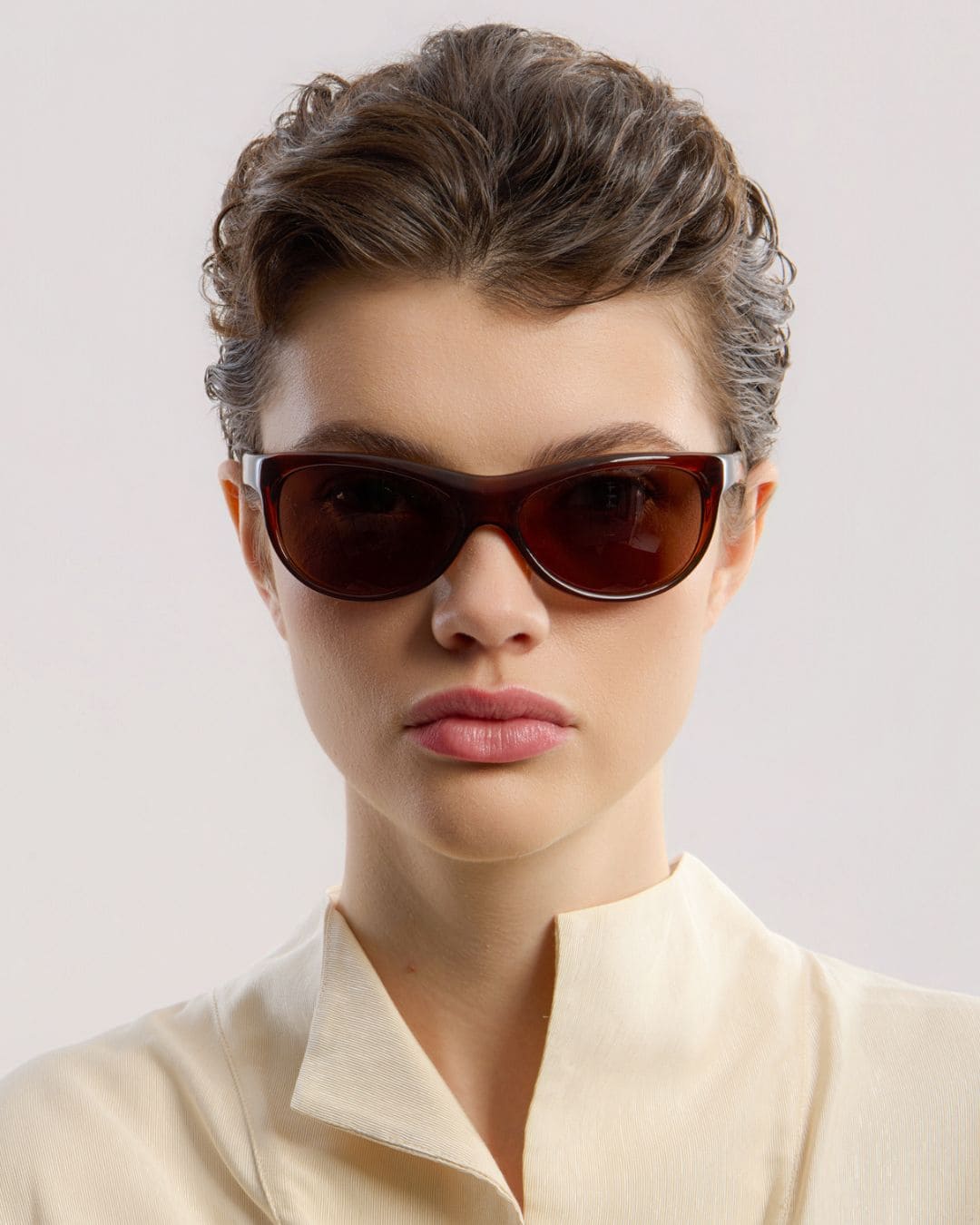 Female model wearing Corlin Eyewear Lynne Brown Brown sunglasses — front view, wraparound acetate frame close-up