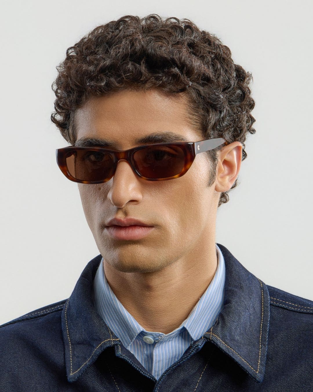 Man wearing tortoise brown sunglasses and a dark jacket with a light background