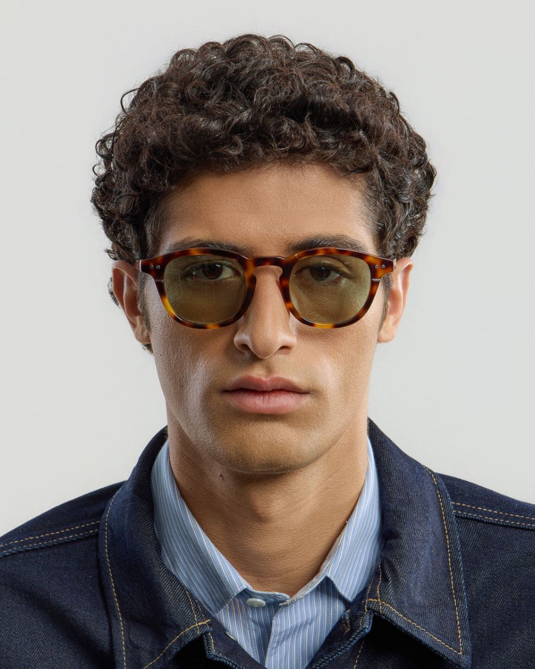 Man wearing tortoise green sunglasses with a neutral background.