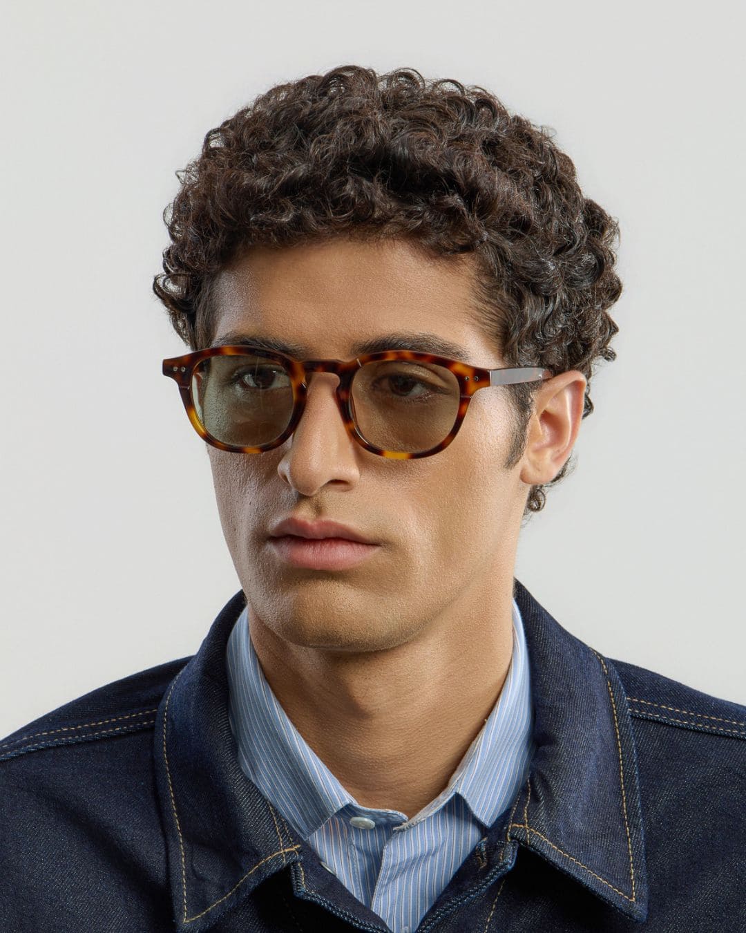 Man wearing tortoise green sunglasses with a neutral background